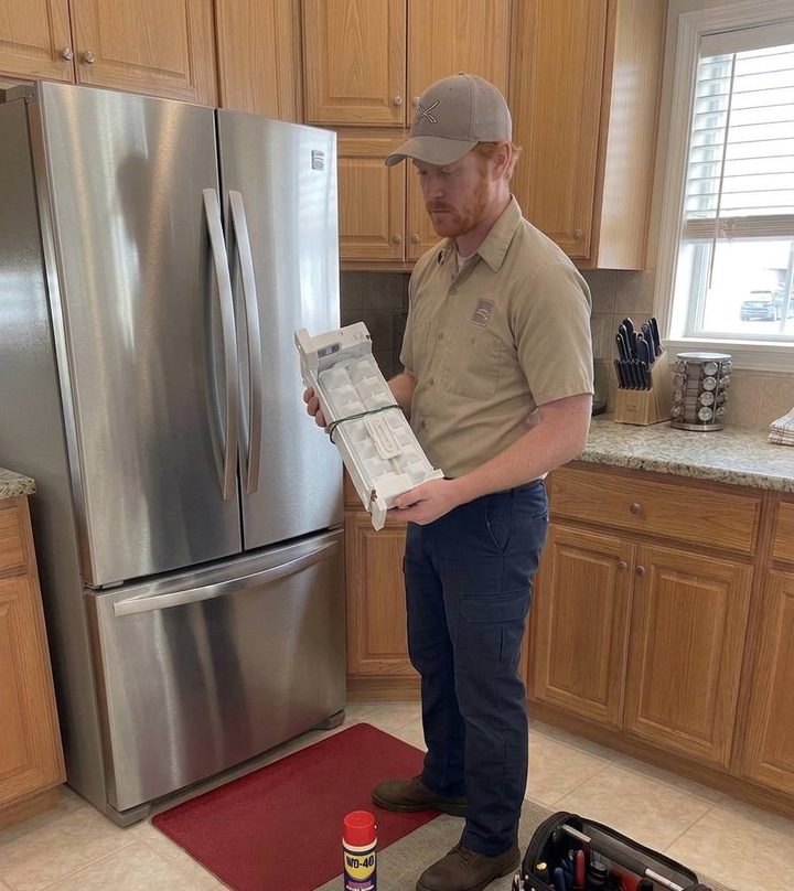 Technician holding an ice maker assembly beside a French-door fridge